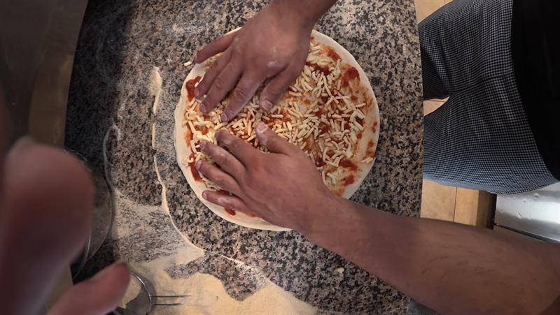 Pizzateig wird auf dem Granit mit Sauce und Käse belegt